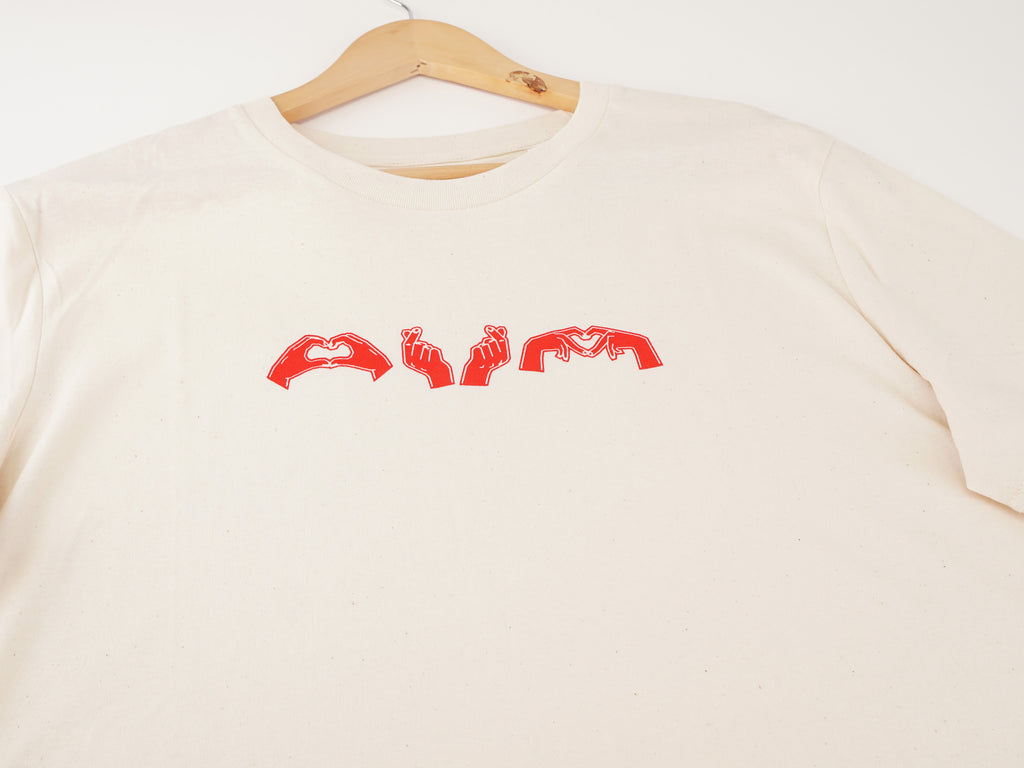 Nahaufnahme des cremeweißen T-Shirts mit rotem Herzgesten-Brustdruck – drei Herzzeichen-Illustrationen auf dem Shirt