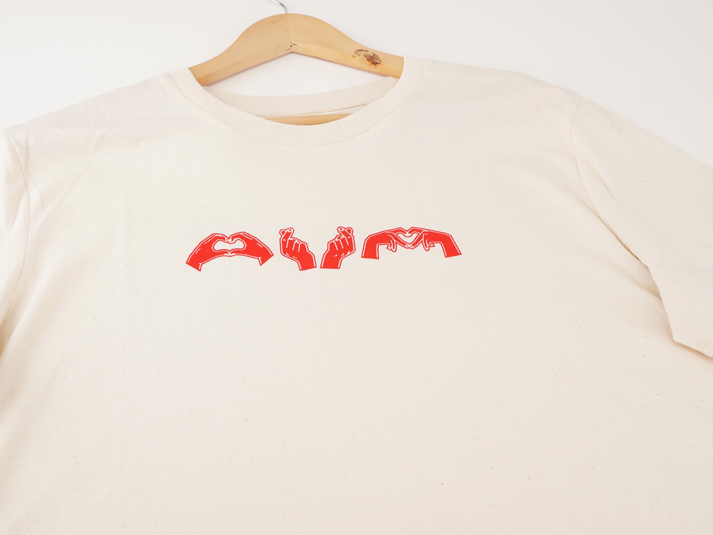 Nahaufnahme des cremeweißen T-Shirts mit rotem Herzgesten-Brustdruck – drei Herzzeichen-Illustrationen auf dem Shirt