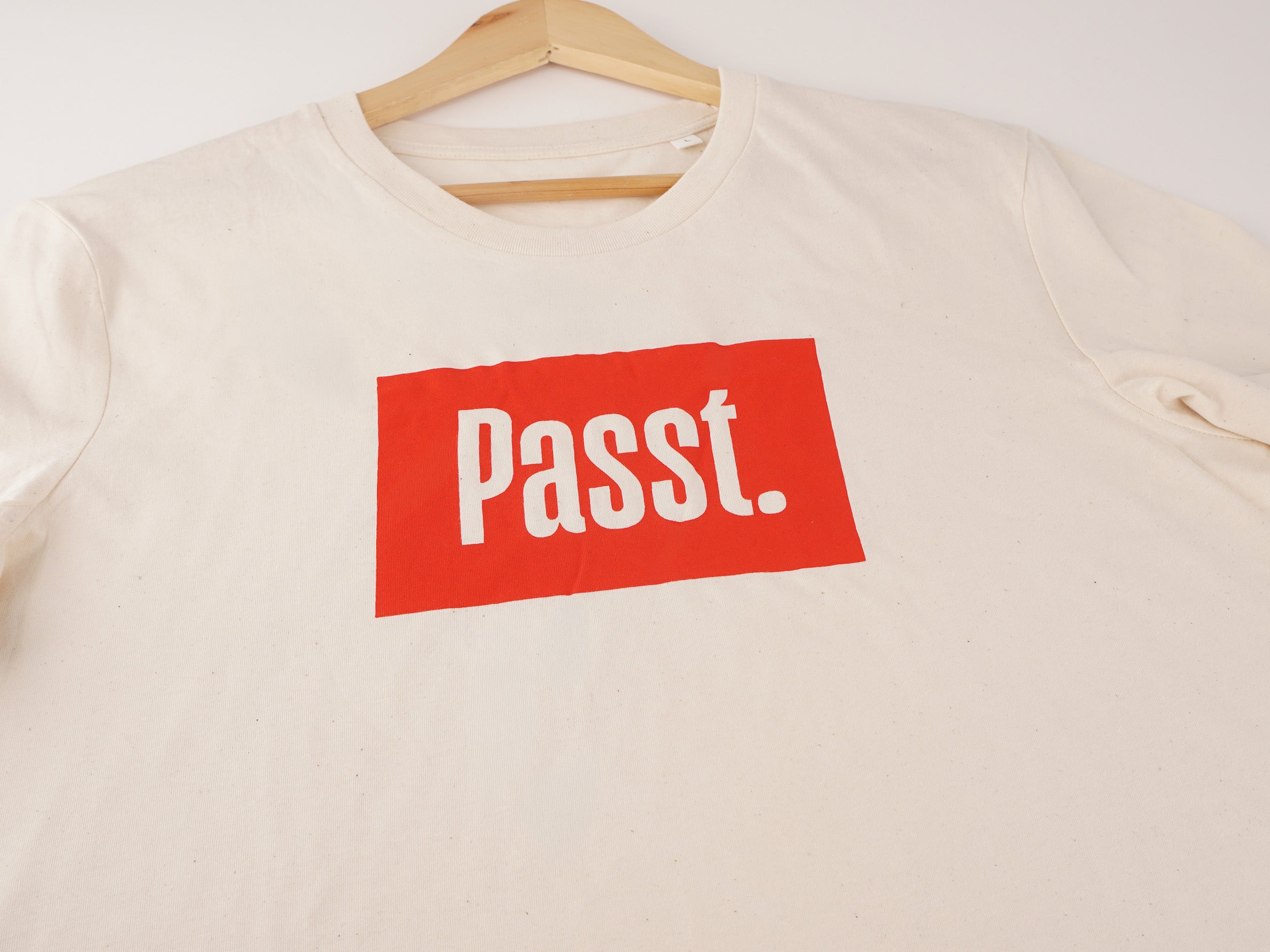 Nahaufnahme des cremeweißen Passt-T-Shirts mit rotem Brustdruck „Passt." – weißer Schriftzug auf rotem Kasten