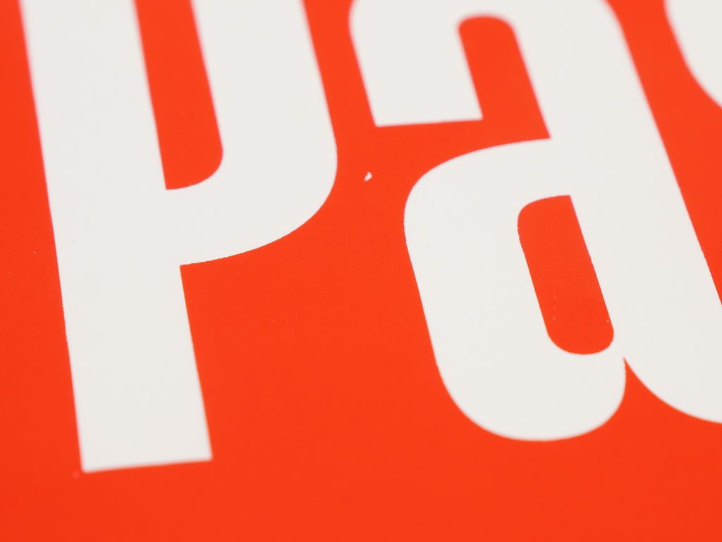 Nahaufnahme des weißen Siebdruckschriftzugs „Passt." auf orangerotem Papier – Typografiedetail