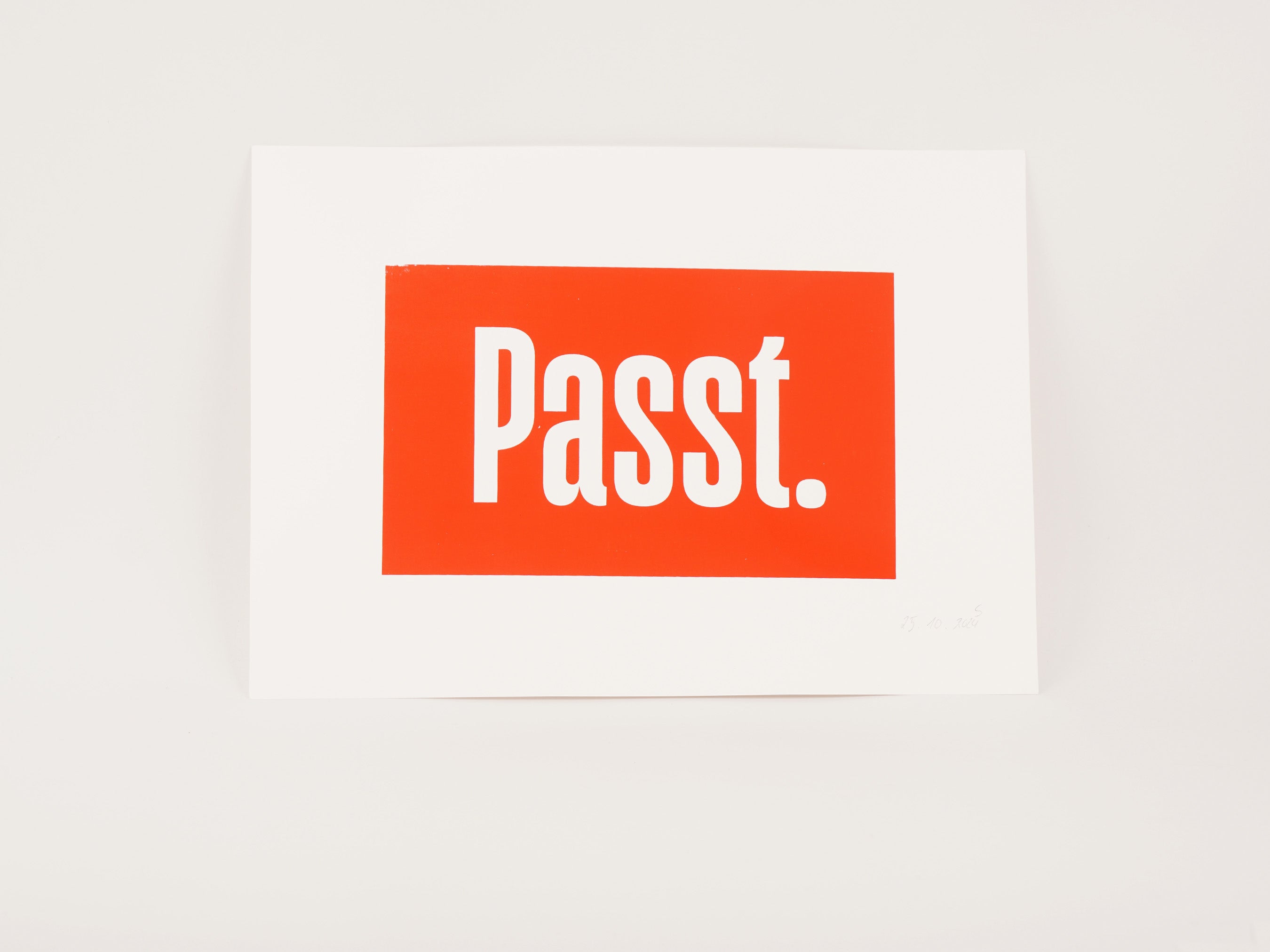 Kunstdruck mit weißem Schriftzug „Passt." auf orangerotem Hintergrund auf Papier