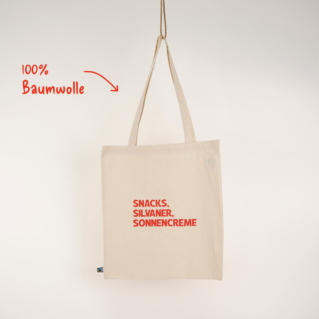 Baumwoll-Jutebeutel mit Aufdruck „SNACKS, SILVANER, SONNENCREME" in Rot, hängend – 100% Baumwolle, Fairtrade-zertifiziert